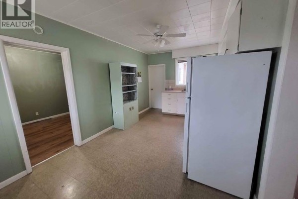 Kitchen area with beige carpet, white cabinets, white refrigerator, and green accent wall. - 6205 97th Street, Osoyoos