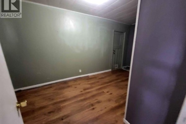 Bedroom with wood laminate flooring and light green walls, featuring a closed door. - 6205 97th Street, Osoyoos