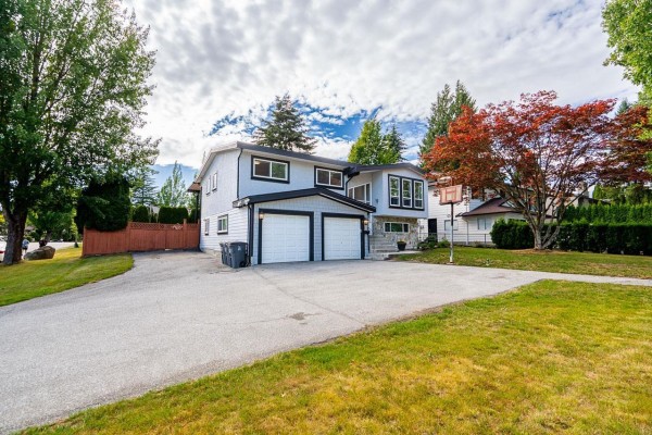 Side exterior view of a light blue two-story house with a grey stone accent wall and two garage doors. - 6209 172 Street, Surrey