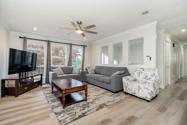 Living room with two grey sofas, armchair, fireplace, and windows looking out to trees. - 6209 172 Street, Surrey