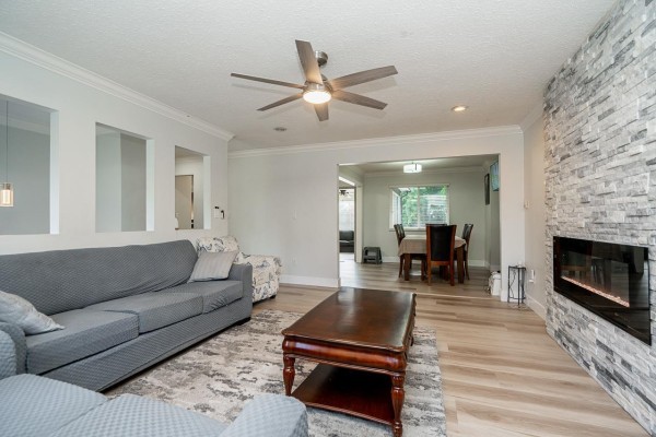 Living room with fireplace, sofa, dining area visible through an open doorway, and wood-look laminate flooring. - 6209 172 Street, Surrey