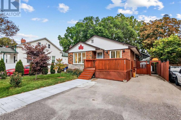 Exterior view of a brick bungalow with a driveway and surrounding homes under a cloudy sky. - 621 Byron Street S, Whitby