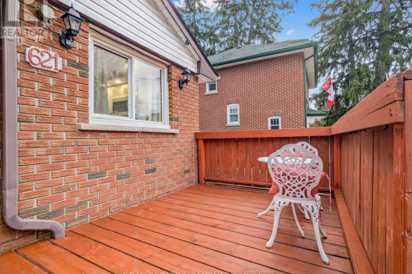 Close-up of a wooden deck with a white metal table and chairs, next to a brick house. - 621 Byron Street S, Whitby
