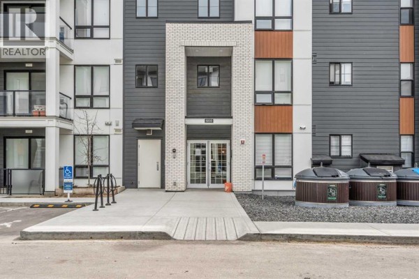 Entrance to a modern apartment building with double glass doors and brick accents. - 6215, 15 Sage Meadows Landing Nw, Calgary