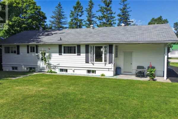 Rear exterior of the white bungalow with a small patio and grassy yard. - 6219 Highway 542, Mindemoya, Manitoulin Island