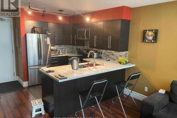 Corner kitchen with dark cabinetry, stainless steel refrigerator, granite island, and bar stools. - 622 - 250 Manitoba Street, Toronto