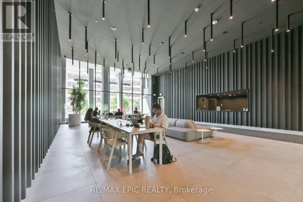 Communal workspace with tables, chairs, sofas, and people working, featuring large windows. - 622 - 500 Wilson Avenue, Toronto