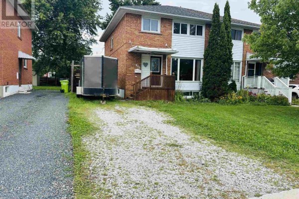 Front view of a two-story house with gravel driveway and trailer. - 622 Placid Ave, Sault Ste Marie