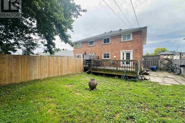 Backyard view with a wooden deck, patio, and green grass. - 622 Placid Ave, Sault Ste Marie