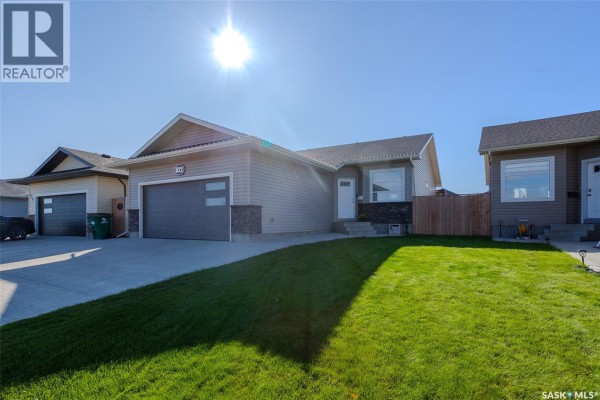 Side view of the beige house with a well-maintained green lawn and a clear blue sky. - 622 Rosewood Boulevard W, Saskatoon