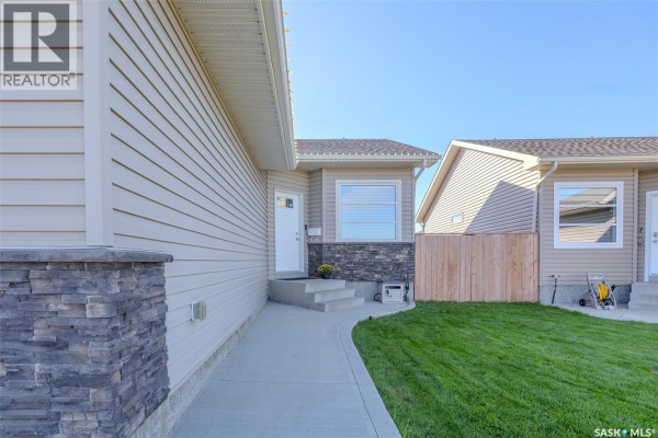 Pathway leading to the front door of a beige house with stone accents and a large window. - 622 Rosewood Boulevard W, Saskatoon