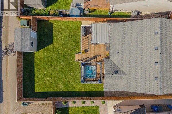 Aerial view of a fenced backyard with a green lawn, wooden deck, and a hot tub. - 622 Rosewood Boulevard W, Saskatoon