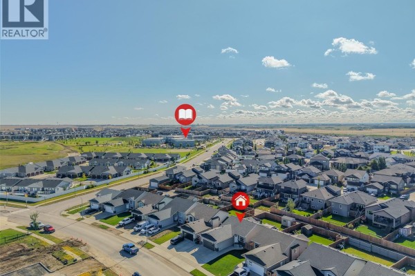 Aerial view of a suburban neighborhood with houses, streets, and a school building in the distance. - 622 Rosewood Boulevard W, Saskatoon