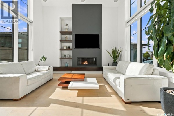 Living room with white sofas, a modern fireplace, mounted TV, and large windows. - 6221 Koep Avenue, Regina