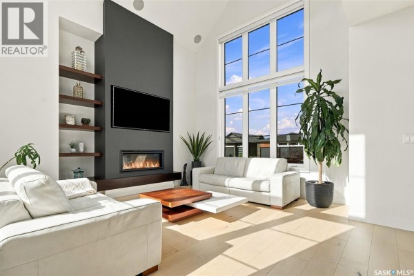 Living room with white sofas, a modern fireplace, mounted TV, and large windows. - 6221 Koep Avenue, Regina