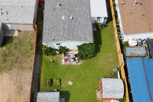 Aerial view of a backyard with a patio, grass, garden beds, and a red shed. - 623 5 Avenue W, Hanna