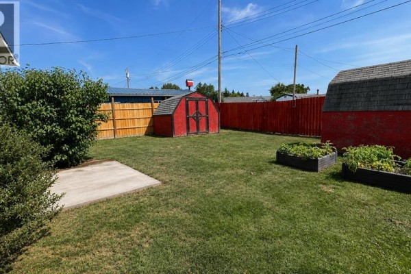 Backyard with a concrete pad, red garden shed, and wooden garden beds. - 623 5 Avenue W, Hanna