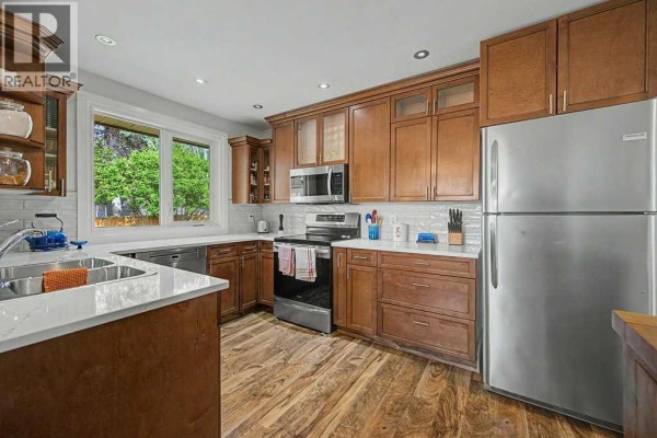 Kitchen view with white quartz countertops, dark wood cabinets, stainless steel appliances, and wood flooring. - 623 Cantrell Place Sw, Calgary