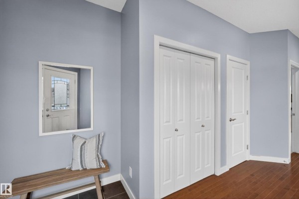 A bright entryway with blue walls, a wooden bench, a mirror, and double closet doors. - 624 Cantor Ld Sw, Edmonton