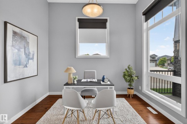 A home office with a desk, chairs, a large window, and wood floors under a fluffy rug. - 624 Cantor Ld Sw, Edmonton
