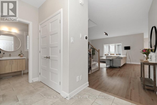 Foyer with light beige tile and hardwood floors, white doors, and view into the living room. - 624 Geneva Crescent, Russell