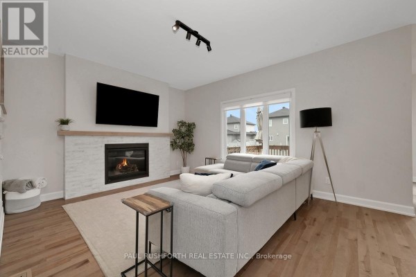 Living room with a gas fireplace, television, light grey sectional sofa, and hardwood floors. - 624 Geneva Crescent, Russell