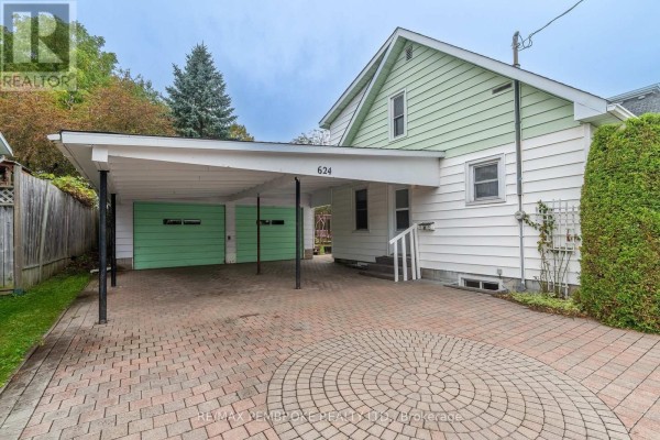 Side exterior of a white house showing a covered carport with two green garage doors and a paved driveway. - 624 Hamilton Street W, Laurentian Valley