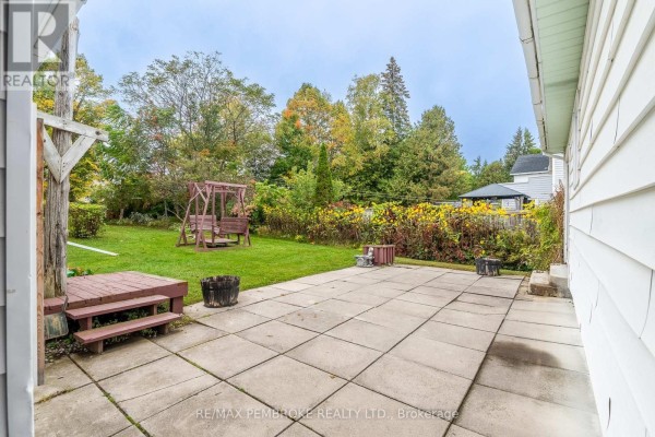Concrete patio in the backyard with a wooden swing set, barrels, and surrounding greenery. - 624 Hamilton Street W, Laurentian Valley