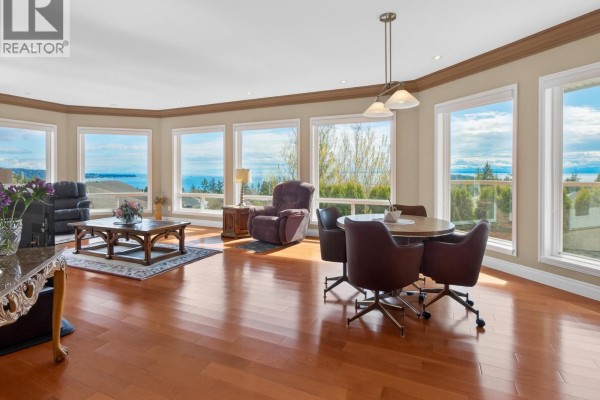 Living and dining area with wood floors, fireplace, and large windows with a view. - 6249 Baillie Road, Sechelt