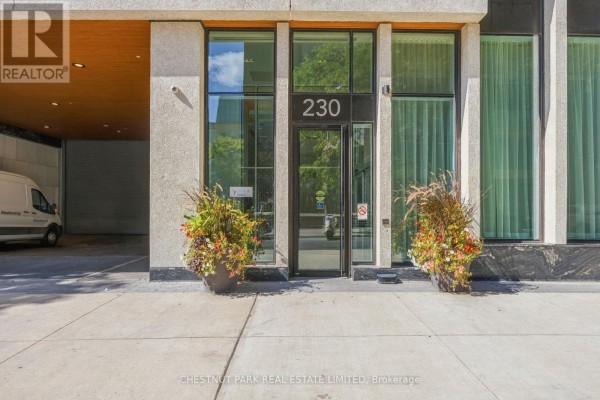 Entrance to the apartment building at 230 Simcoe Street, with glass doors and planters. - 625 - 230 Simcoe Street, Toronto