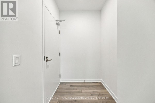 Hallway inside the apartment with a white door, chrome handle, and wood-look flooring. - 625 - 230 Simcoe Street, Toronto