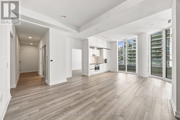 Open-concept living space with kitchen, light wood floors, and large windows overlooking the city. - 625 - 230 Simcoe Street, Toronto