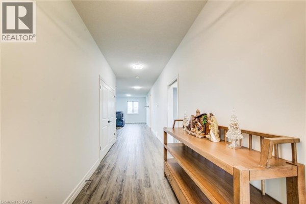 Long, bright hallway with white walls, grey wood-look flooring, and a console table. - 625 Winchester Avenue S, Listowel