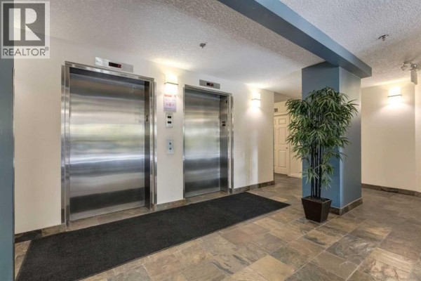 Interior hallway with two stainless steel elevators, tiled floor, and decorative plant. - 626, 930 Centre Avenue Ne, Calgary