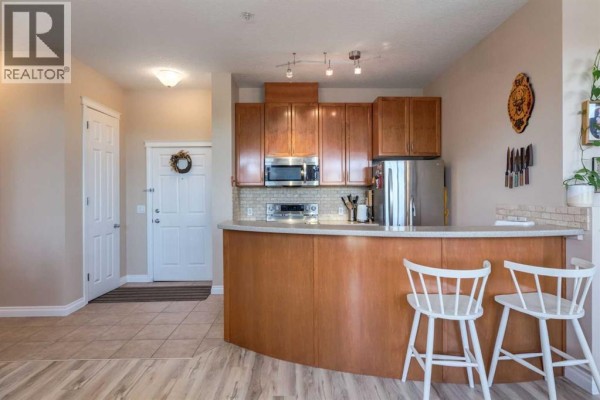 Kitchen area with wood cabinets, stainless steel appliances, and a curved breakfast bar with stools. - 626, 930 Centre Avenue Ne, Calgary
