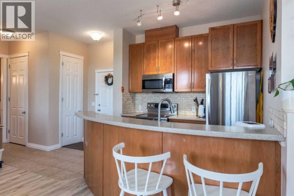 Kitchen area with wood cabinets, stainless steel appliances, and a curved breakfast bar with stools. - 626, 930 Centre Avenue Ne, Calgary
