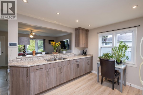 Kitchen with dual sinks, wood-grain cabinetry, granite countertops, and a view into the living room. - 626 16th St, Courtenay
