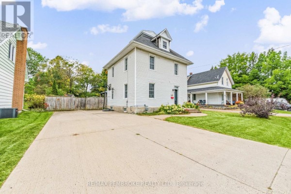 Concrete driveway leading to the side of a white two-story house with green lawn and trees. - 626 Hamilton Street W, Laurentian Valley