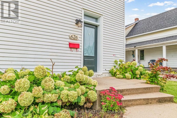 Close-up of the front entrance of a white house, showing a dark green door, concrete steps, and flowering bushes. - 626 Hamilton Street W, Laurentian Valley