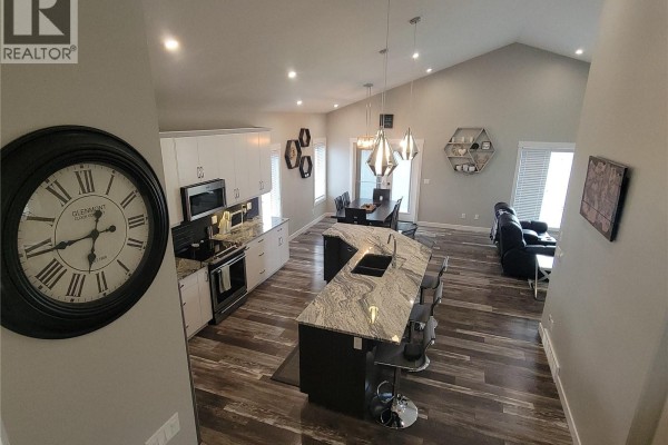 Open-concept living and dining area with a fireplace, large windows, and a kitchen island with pendant lights. - 626 Kinloch Crescent, Saskatoon