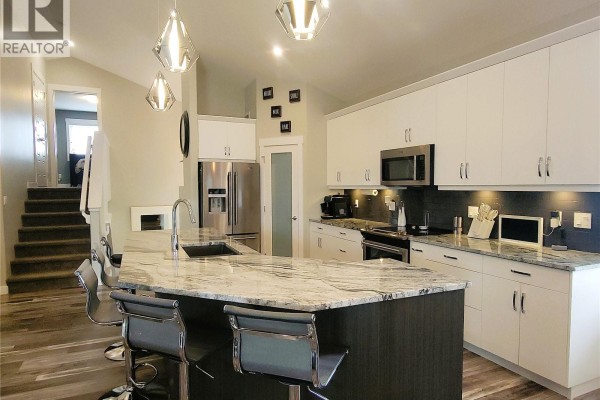Kitchen featuring white cabinetry, stainless steel appliances, a granite island with bar stools, and a view of the stairs. - 626 Kinloch Crescent, Saskatoon