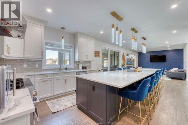 Long kitchen island with blue velvet chairs, white cabinets, and a tiled backsplash. - 6275 Disputed Rd., Lasalle