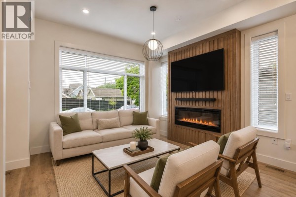 Living room featuring a sofa, chairs, electric fireplace, and large windows overlooking the street. - 6280 Wales Street, Vancouver