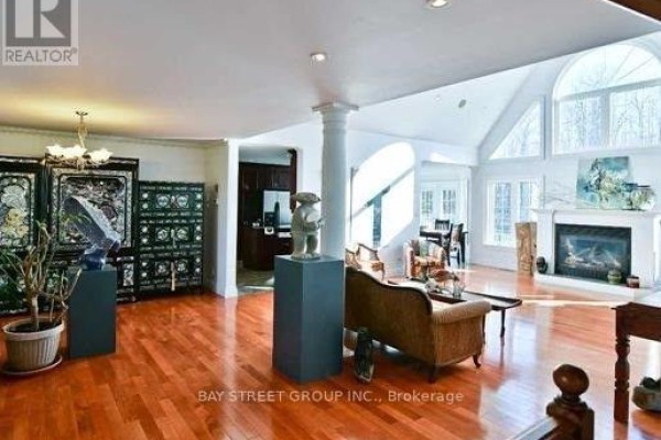 Spacious living area with polished wood floors, a fireplace, vaulted ceiling, and large windows. - 6289 Black River Road, Georgina