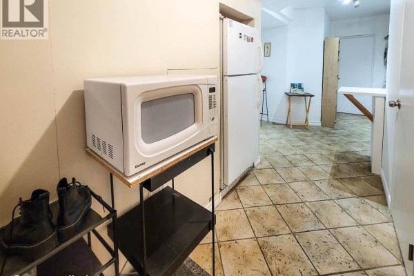 Kitchen area with a white refrigerator, microwave on a black stand, and tiled floor. - 628x Elliott St, Vancouver