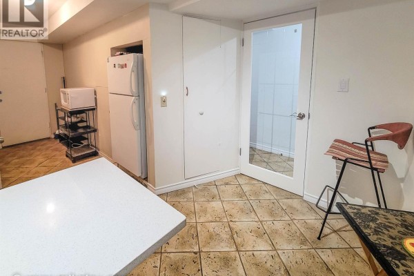 Kitchenette with a refrigerator, microwave, tiled floor, white cabinets, and a stool by a counter. - 628x Elliott St, Vancouver