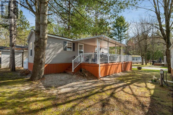 Side exterior of a grey mobile home with a covered deck and white railings. - 63 - 1082 Shamrock Marina Road, Gravenhurst