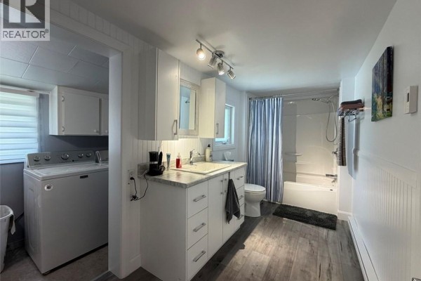 Bathroom with a vanity, toilet, bathtub with shower curtain, and laundry machines to the left. - 63 42e Avenue, Edmundston