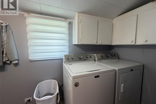 Laundry area with a white washing machine and dryer, grey walls, white cabinets, and a window. - 63 42e Avenue, Edmundston