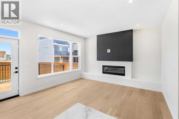 Living area with a contemporary gas fireplace, white walls, and light wood flooring. - 63 Annette Rise Nw, Calgary